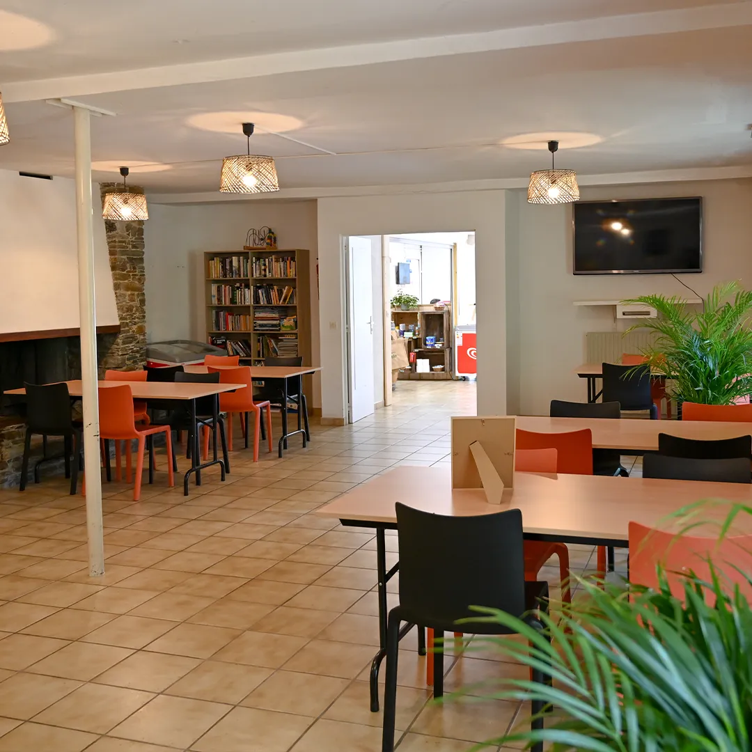 Salle polyvalente du camping avec tables, coin bibliothèque et télévision